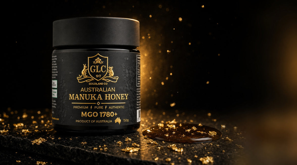 A 150 g matte black jar of Goldland Co. Australian Manuka Honey MGO 1780+ on dark polished stone, lit from behind with gold leaf flakes scattered across a pool of honey.